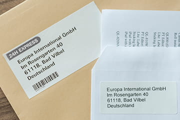 Brother DK die-cut label next to a Brother DK continuous length label stuck to envelopes
