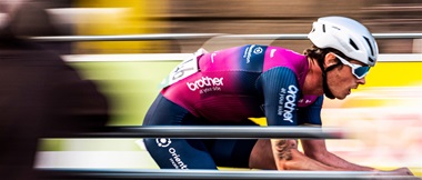 Cyclist from Brother UK backed, Crimson Performance team, riding past spectators in a blur