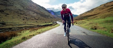 Cyclist Joey Walker riding towards the camera, along an unmarked road  with mountainous terrain to the sides and in the background