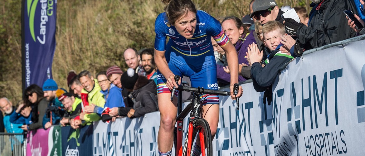 Cyclist Rebecca Richardson approaching the finish line of a hill climb with spectators cheering her on