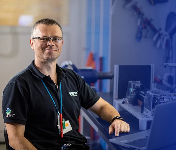 A man sat wearing a blue t-shirt in front of a laptop surrounded by tools