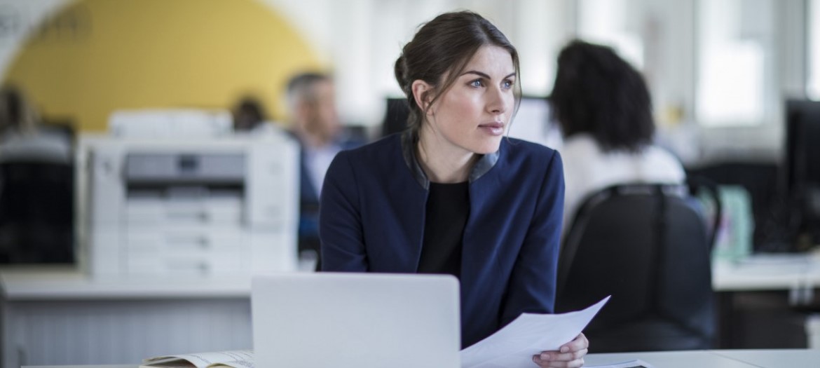 A woman in an office who is wearing a blue jacket and looking off to the side