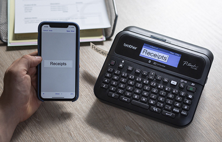 Female office worker sat on office desk with file folder in hand, next to a PC and Brother P-touch label printer